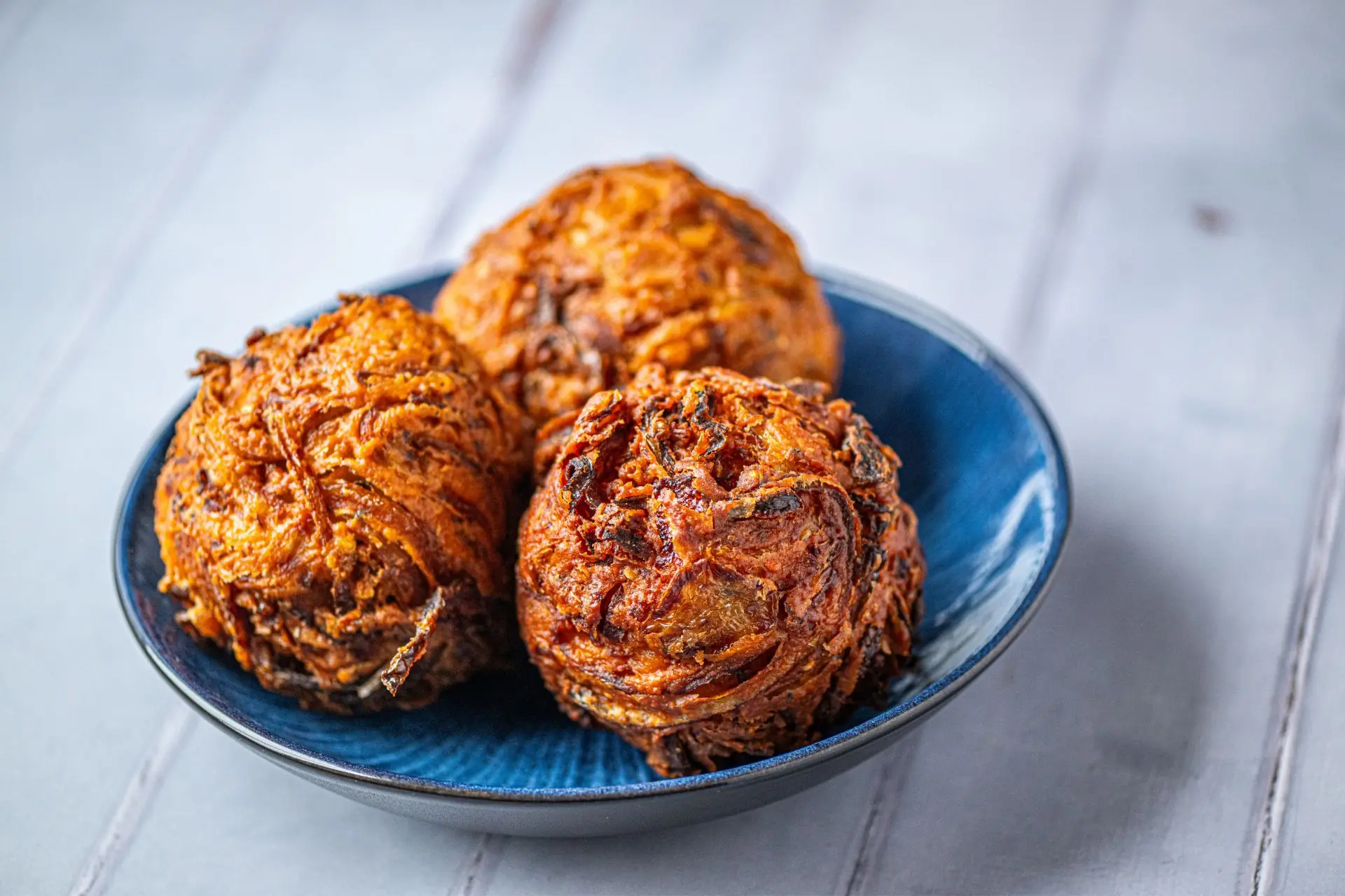 Crispy handmade golden onion bhajis served in a blue bowl | Alvi's Homemade